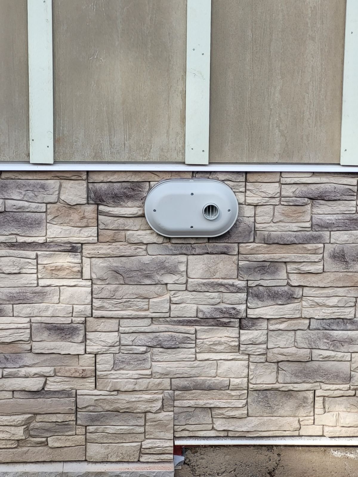 Exterior vent termination cap on a stone veneer wall